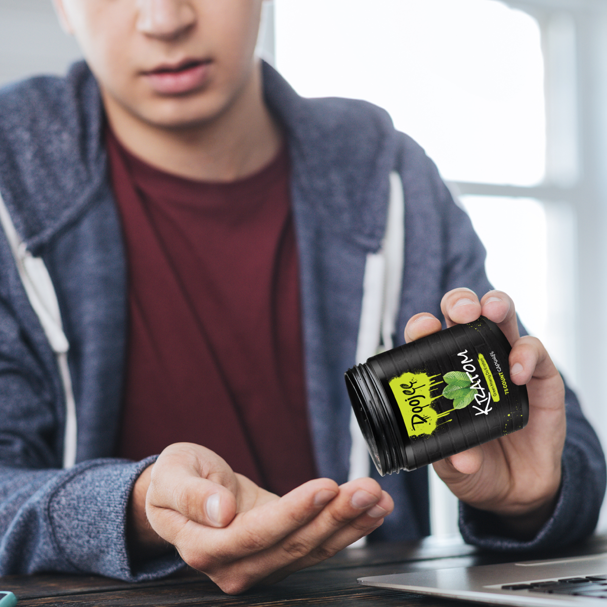 A person holds a black container labeled "Kratom" and gestures toward their outstretched palm